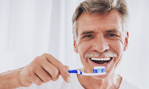 older man in white shirt brushing his teeth 