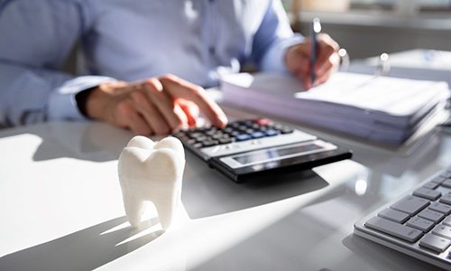 A man sitting at a desk with a calculator and a model of a tooth