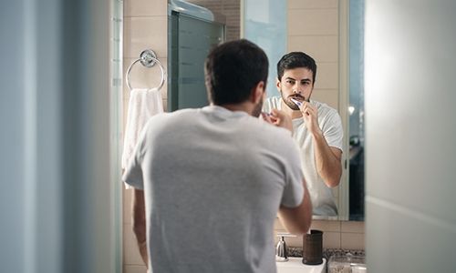 A young man standing in front of the mirror brushing his teeth
